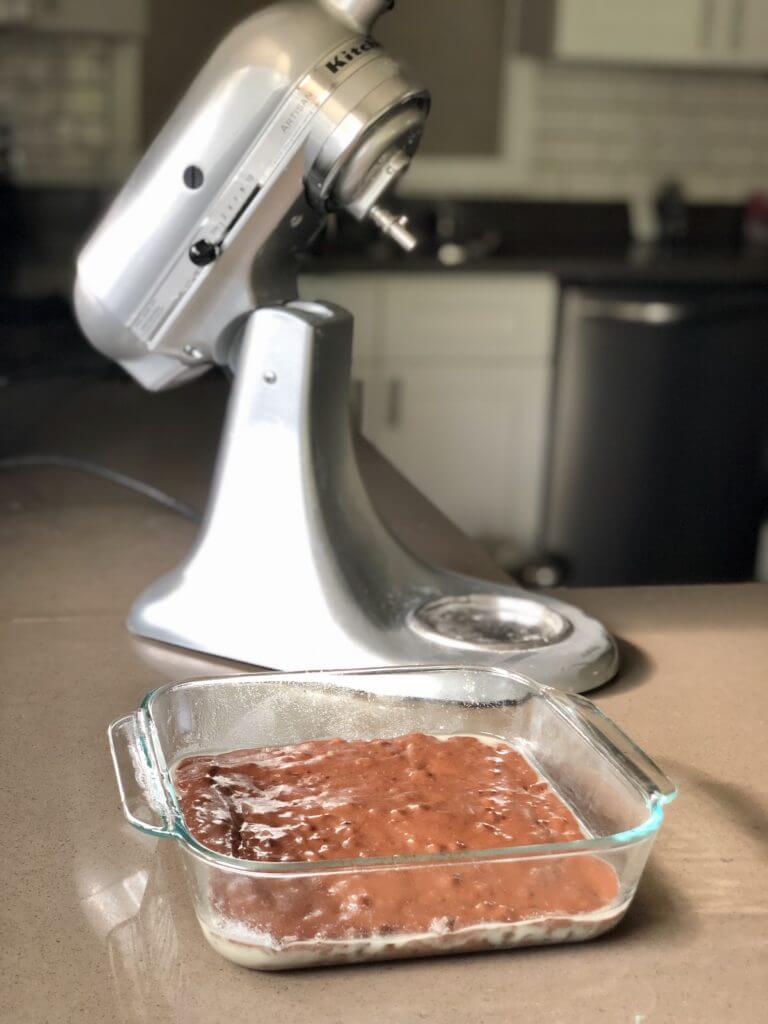 mixer in the background and uncooked brownies in a pan in the forefront