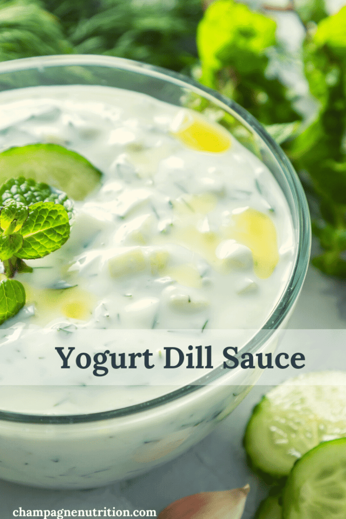 A glass bowl of creamy, white sauce with cucumber and dill
