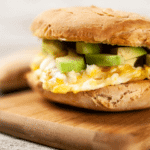 a fluffy egg sandwich on a golden bun with greens and avocado