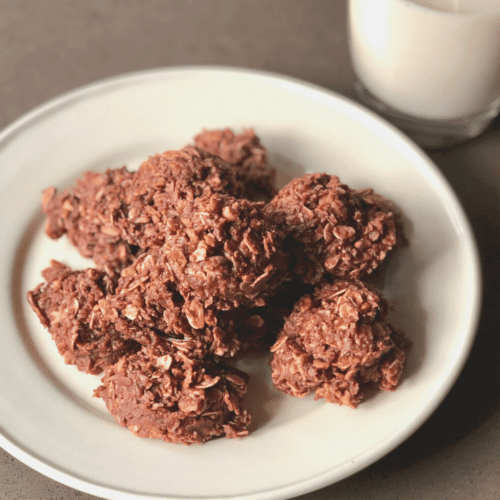 A stack of no-bake vegan cookies on a white plate with non-dairy milk in the background