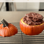 A chocolate cake baked in a pumpkin cooling on a rack